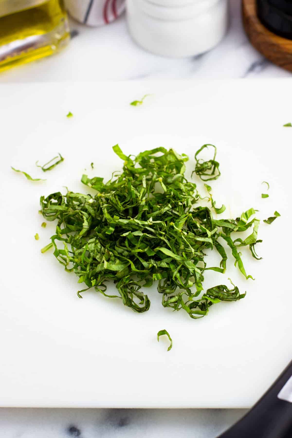 Chiffonade cut basil on a cutting board.