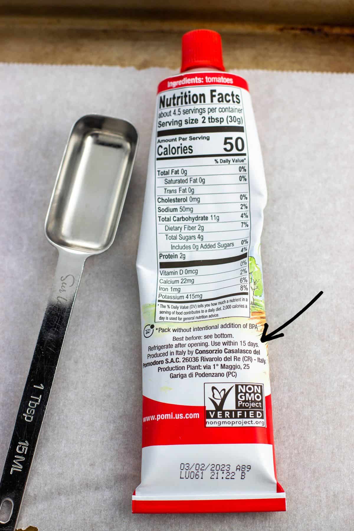 A tablespoon and tube of tomato paste on a baking sheet.