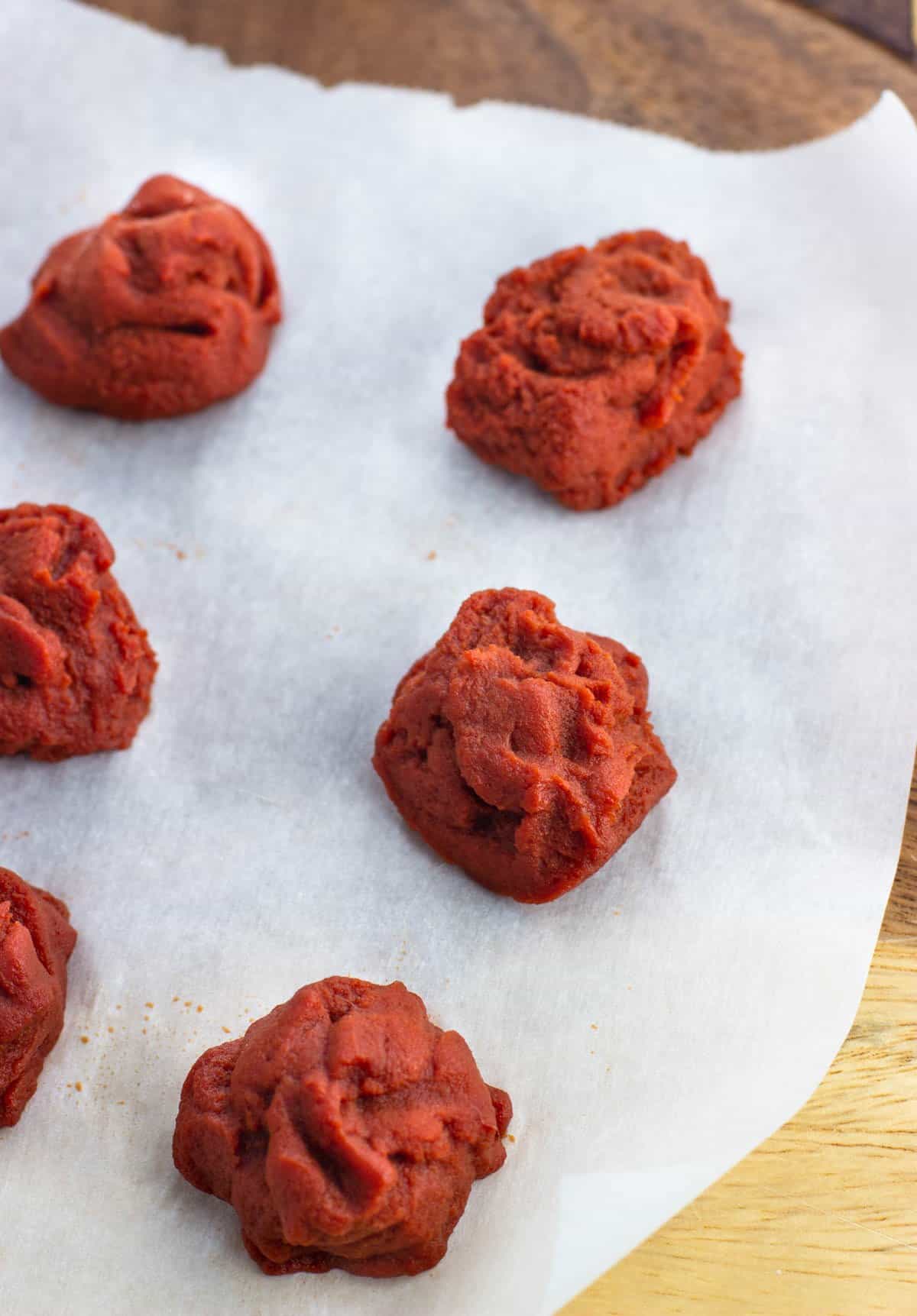 Six tomato paste tablespoons on a sheet of parchment paper.