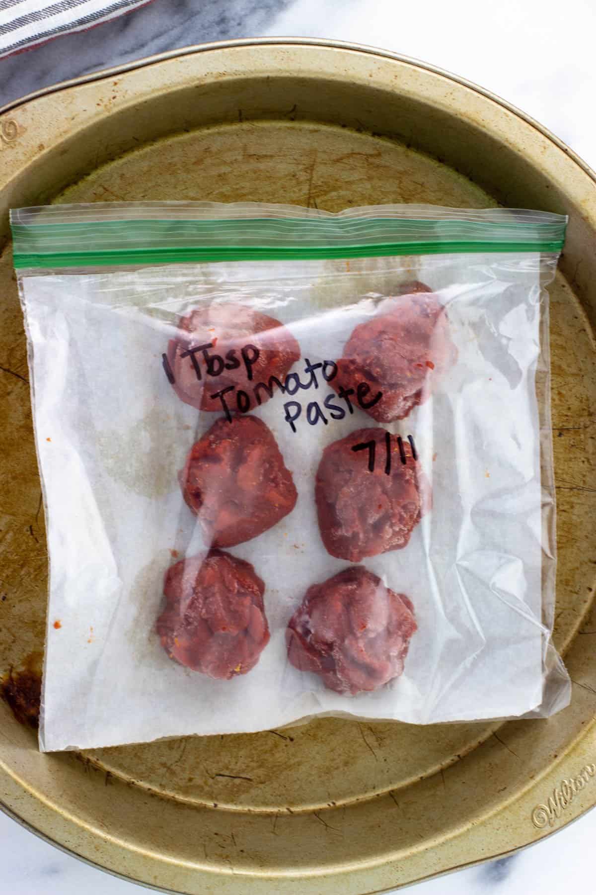 Frozen tomato paste blobs in a labeled plastic bag.