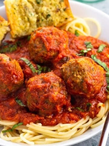 A shallow bowl of spaghetti and sausage meatballs with garlic bread.