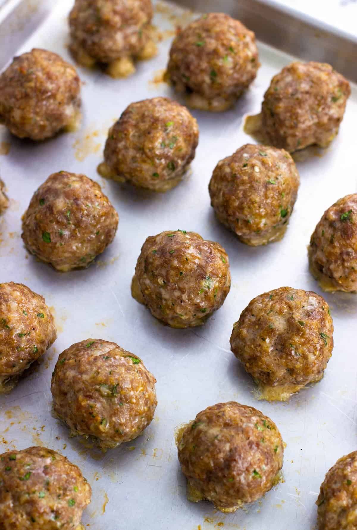 Baked sausage meatballs on a large baking sheet.