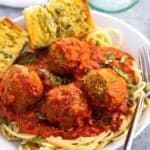 A shallow bowl of spaghetti and sausage meatballs with garlic bread.