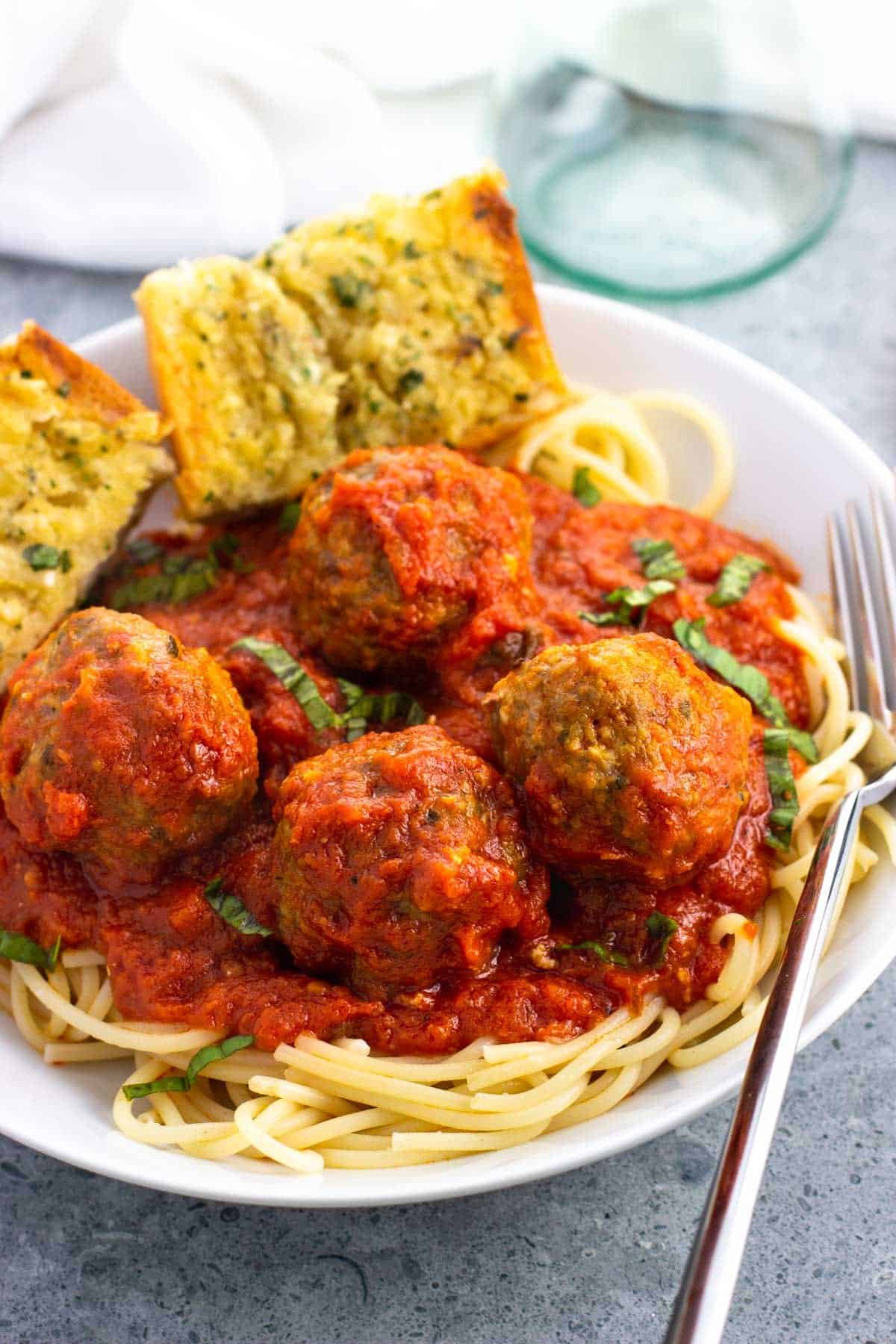 A shallow bowl of spaghetti and sausage meatballs with garlic bread.