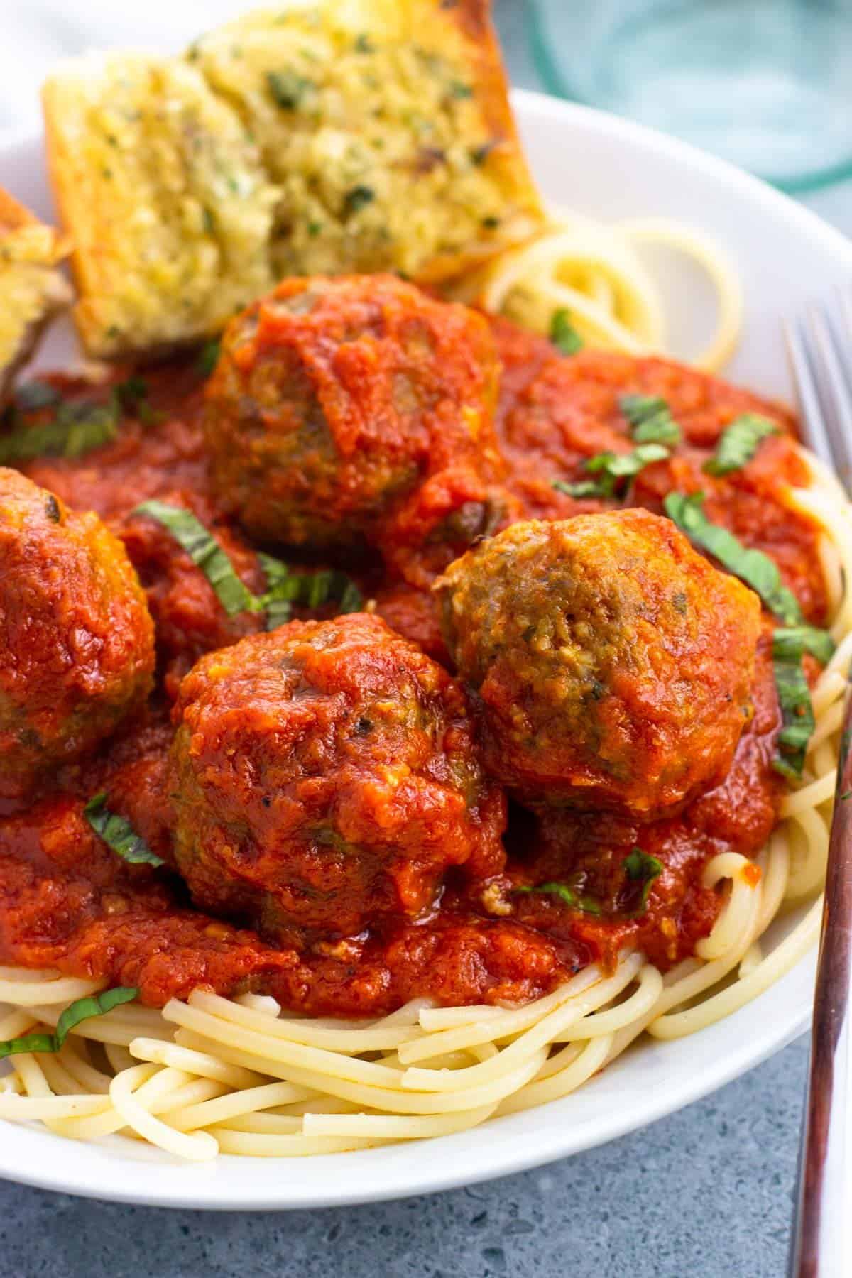 A shallow bowl of spaghetti and sausage meatballs with garlic bread.