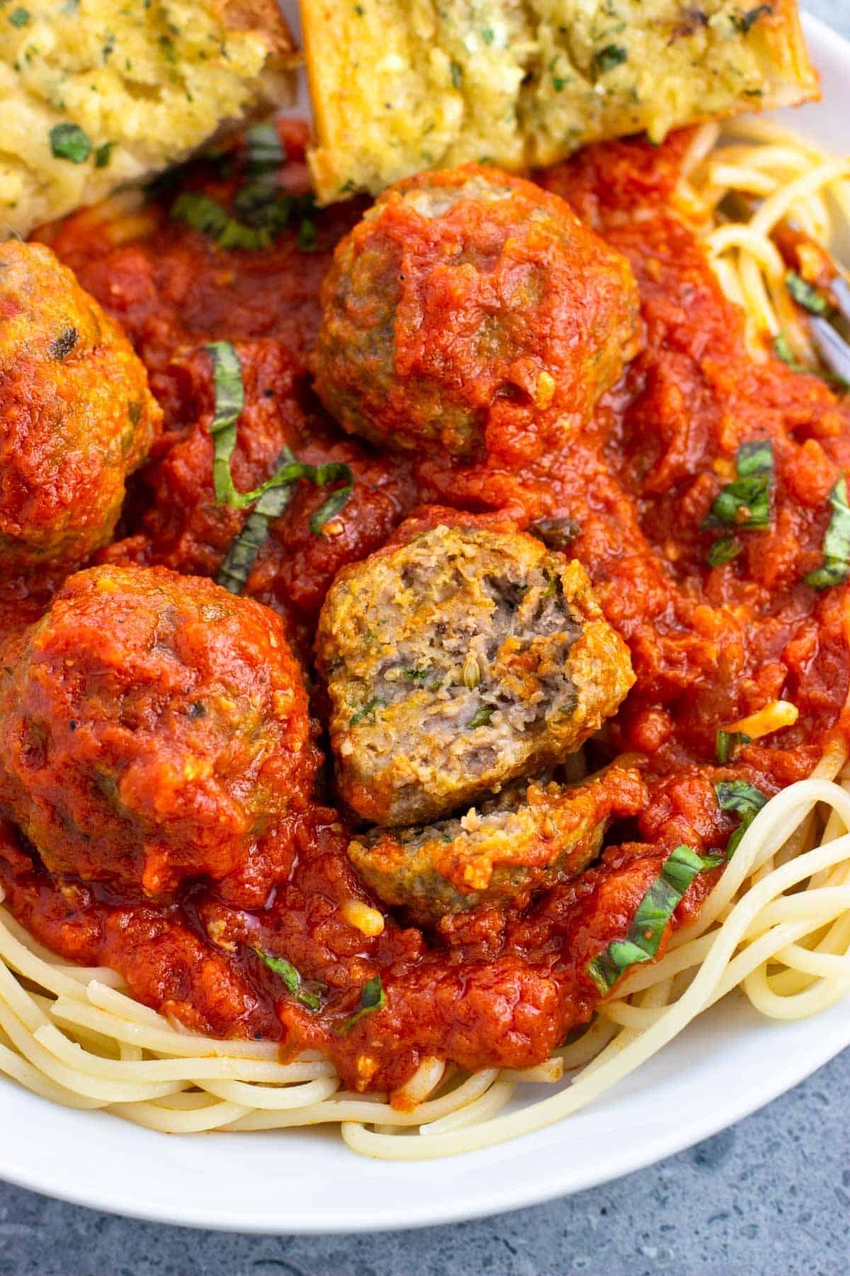 A bowl of spaghetti and meatballs with one meatball cut in half.