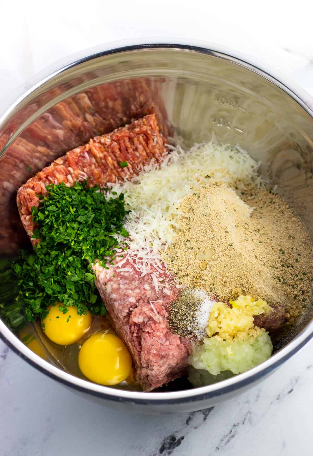 All meatball ingredients added to a large metal mixing bowl.