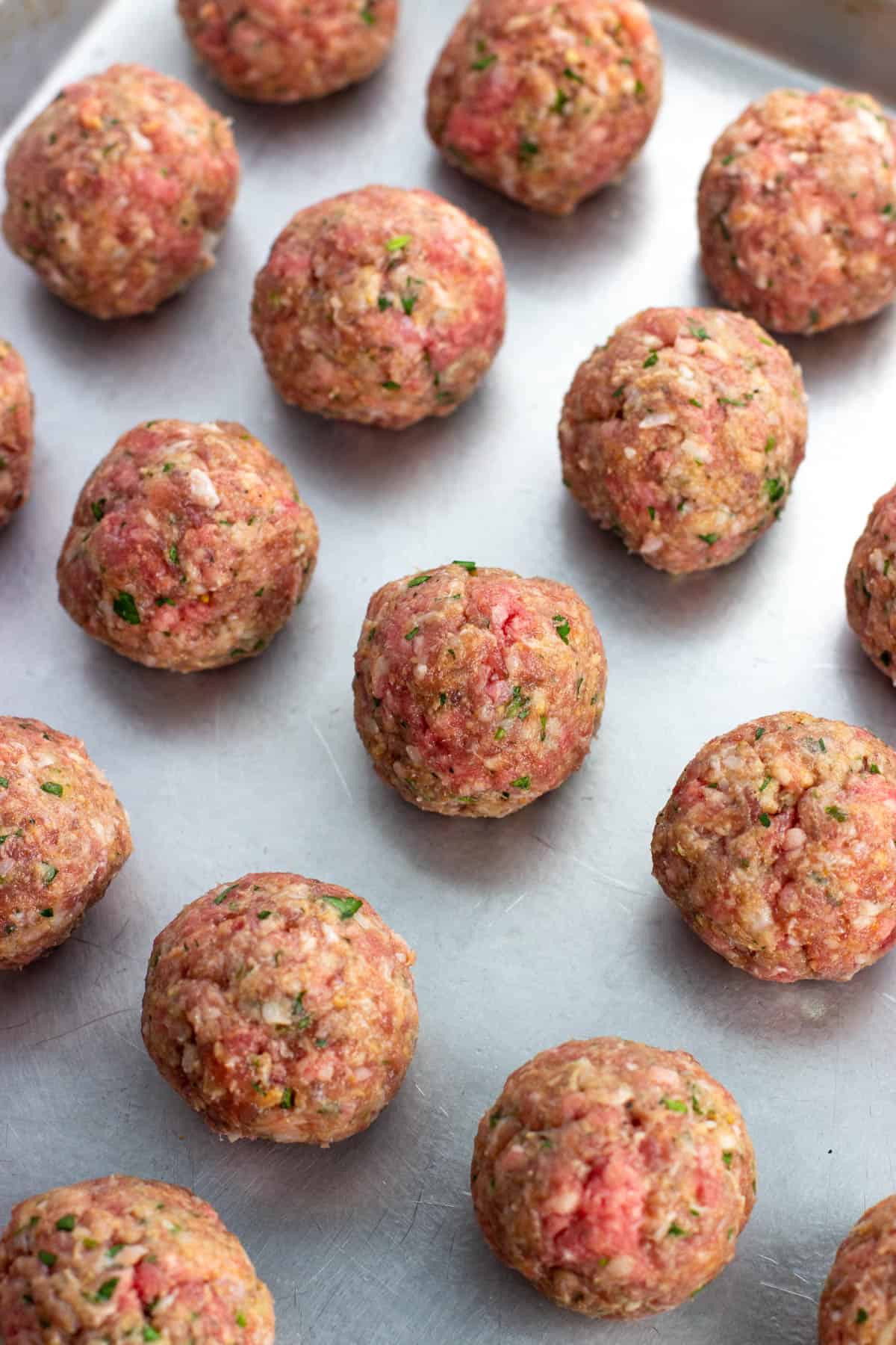 Rolled raw meatballs on a sheet pan.