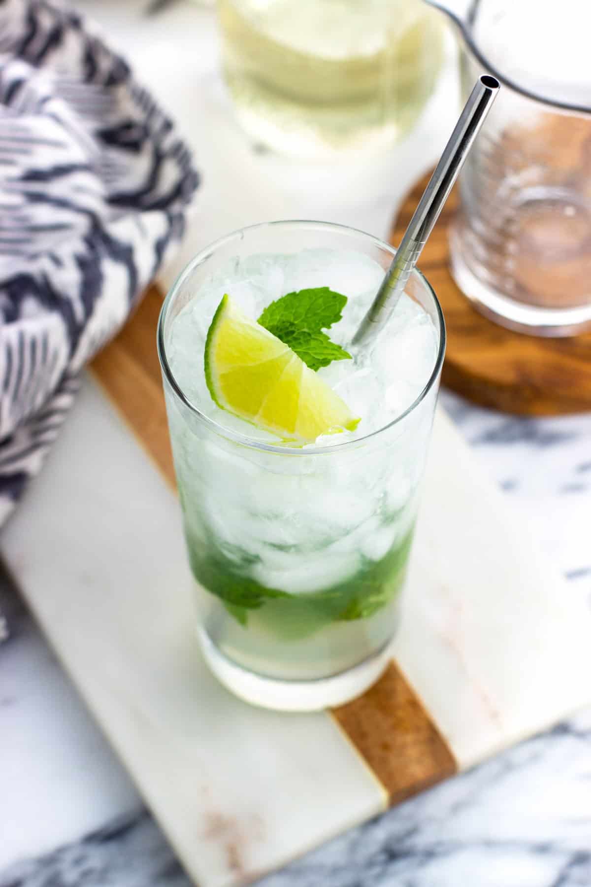 A virgin mojito garnished with lime and mint leaves with a metal straw.