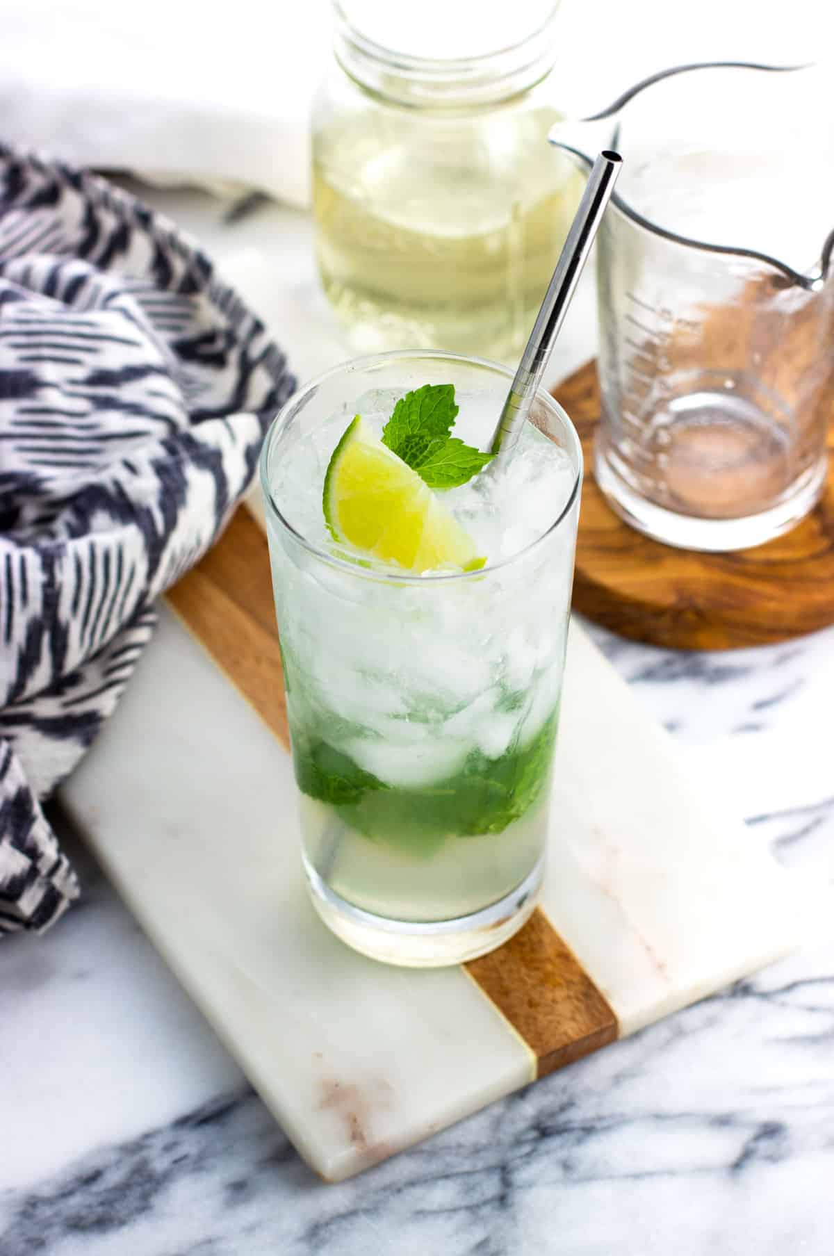 A mojito mocktail garnished with lime and mint leaves with a metal straw.