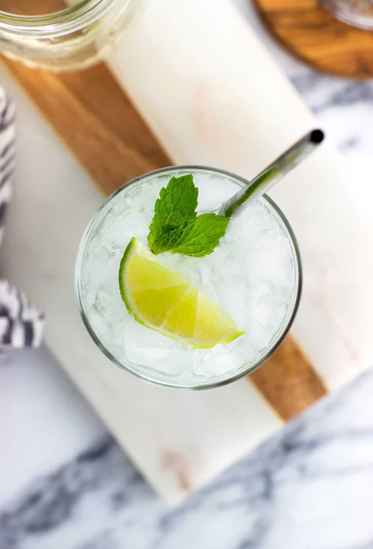 A top view of a mojito mocktail garnished with lime and mint leaves with a metal straw.