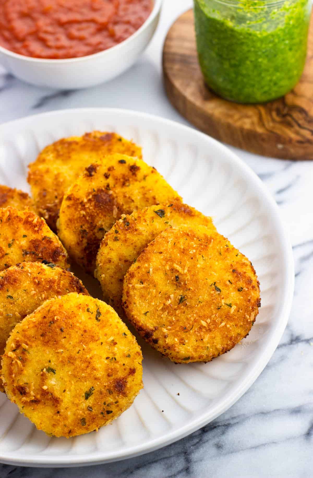 Slices of polenta served on a plate next to pesto and marinara sauce.