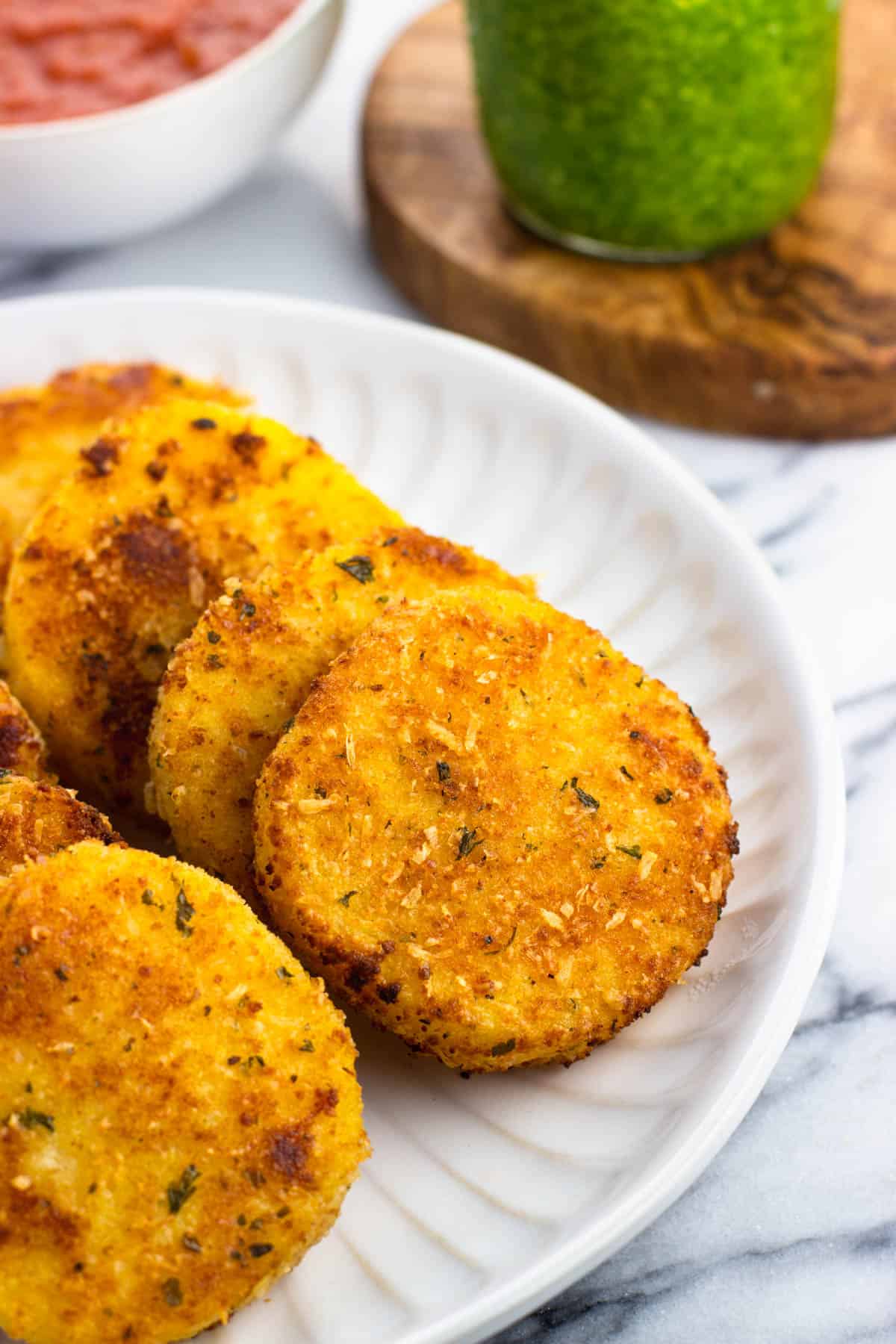 Slices of polenta served on a plate next to pesto and marinara sauce.