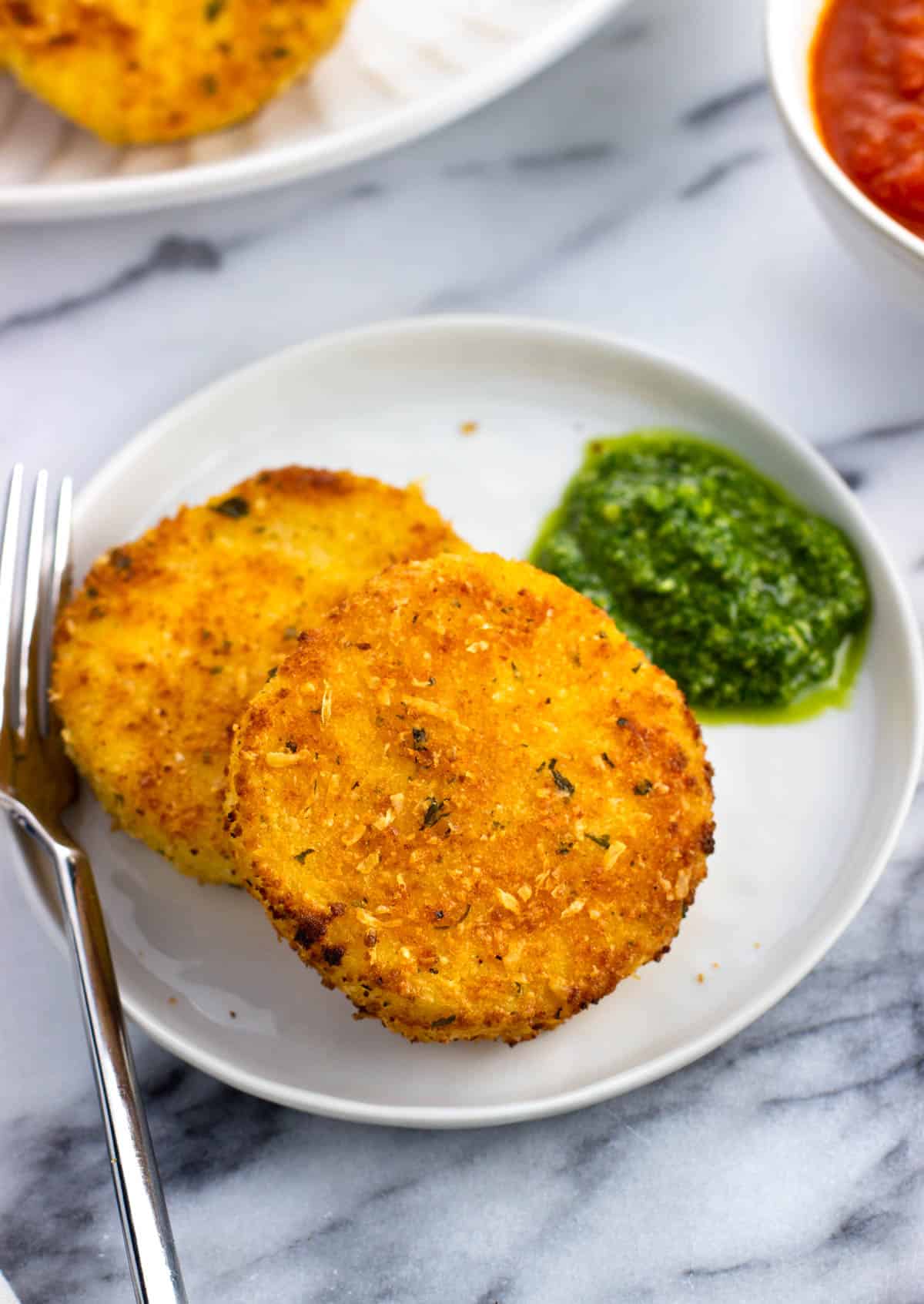 Two fried polenta slices on a plate with a dollop of pesto.