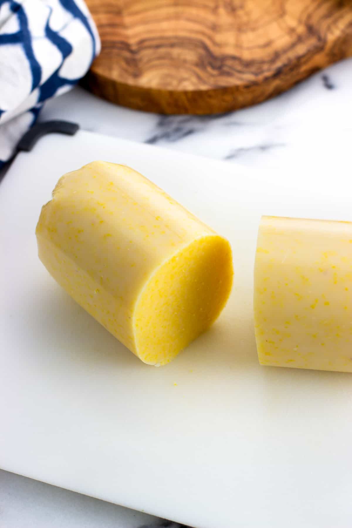 A tube of polenta sliced in half on a cutting board.