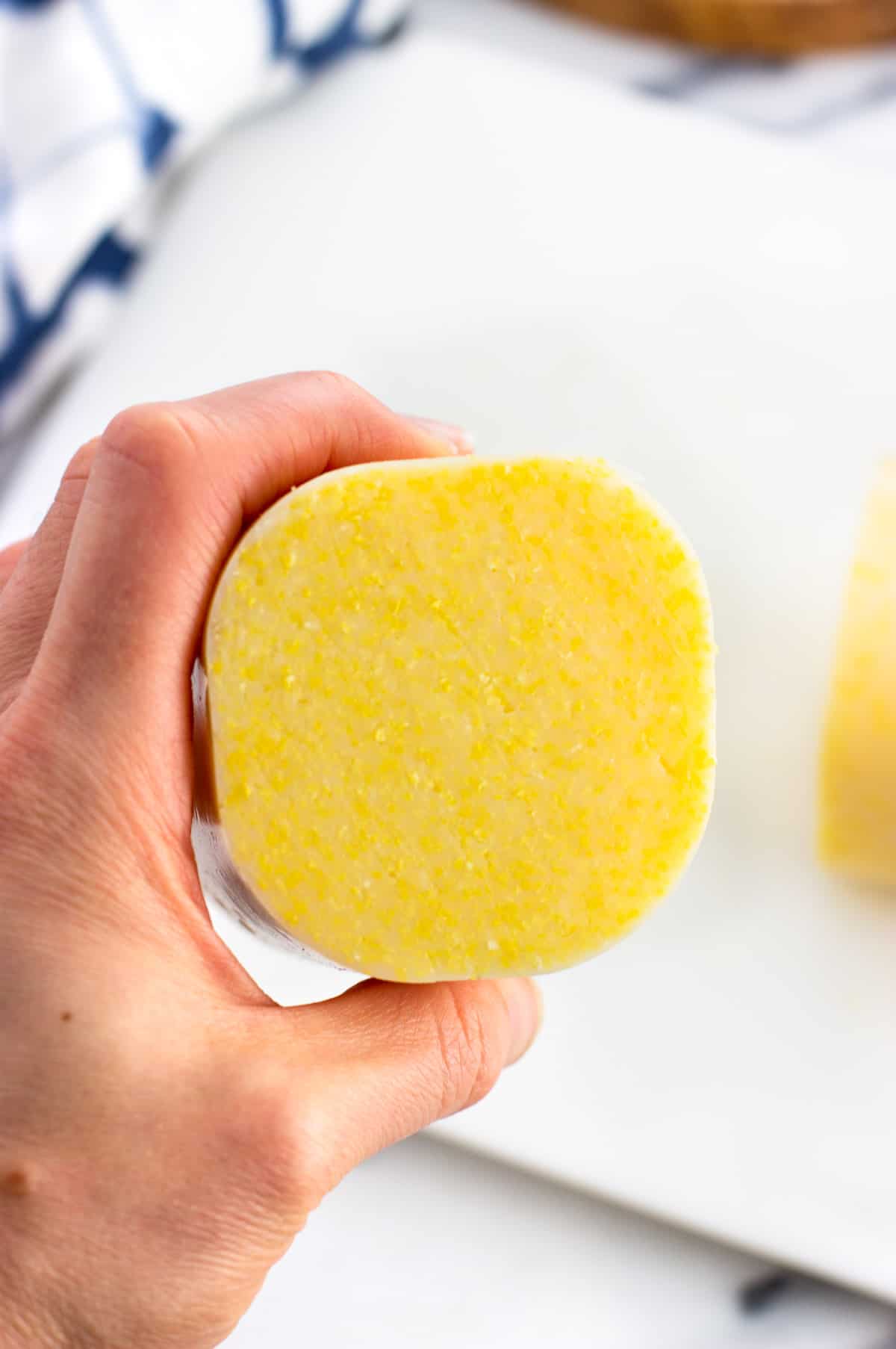 A hand holding up a sliced tube of polenta to show the inner texture.