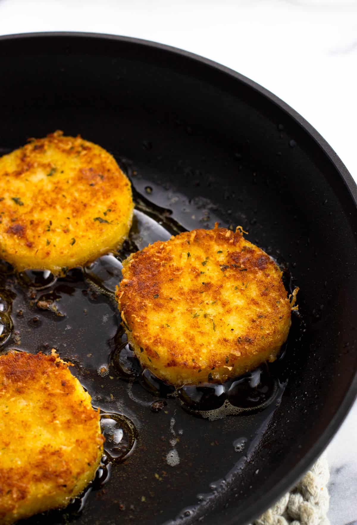 Breaded polenta slices being pan fried in a skillet.