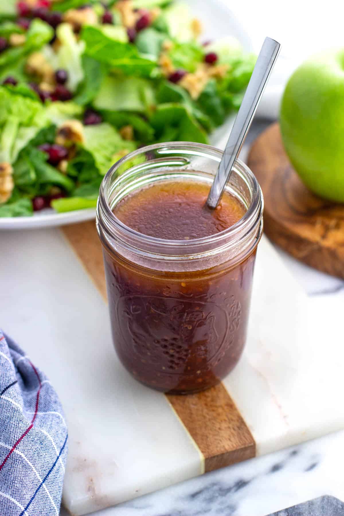 A glass jar of pomegranate vinaigrette in front of salad.