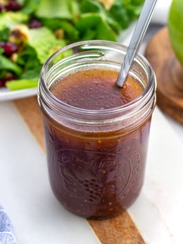 A jar of pomegranate vinaigrette with a spoon in it.