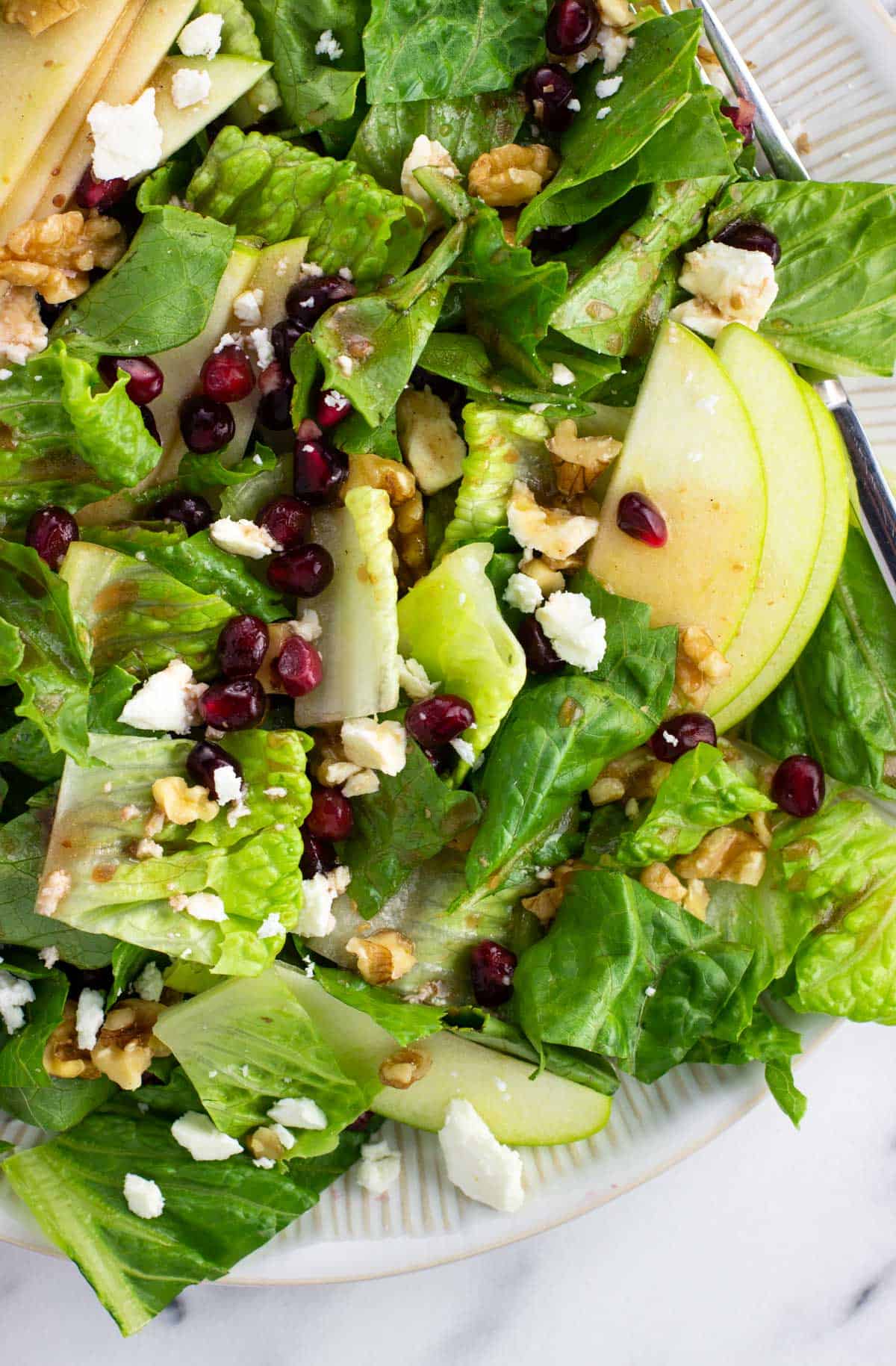 A salad topped with pomegranate vinaigrette, feta, apple slices, walnuts, and pomegranate arils.