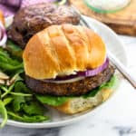 A portobello mushroom burger topped with cheese and red onion on a plate with a salad.