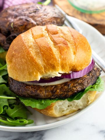 A portobello mushroom burger topped with cheese and red onion on a plate with a salad.