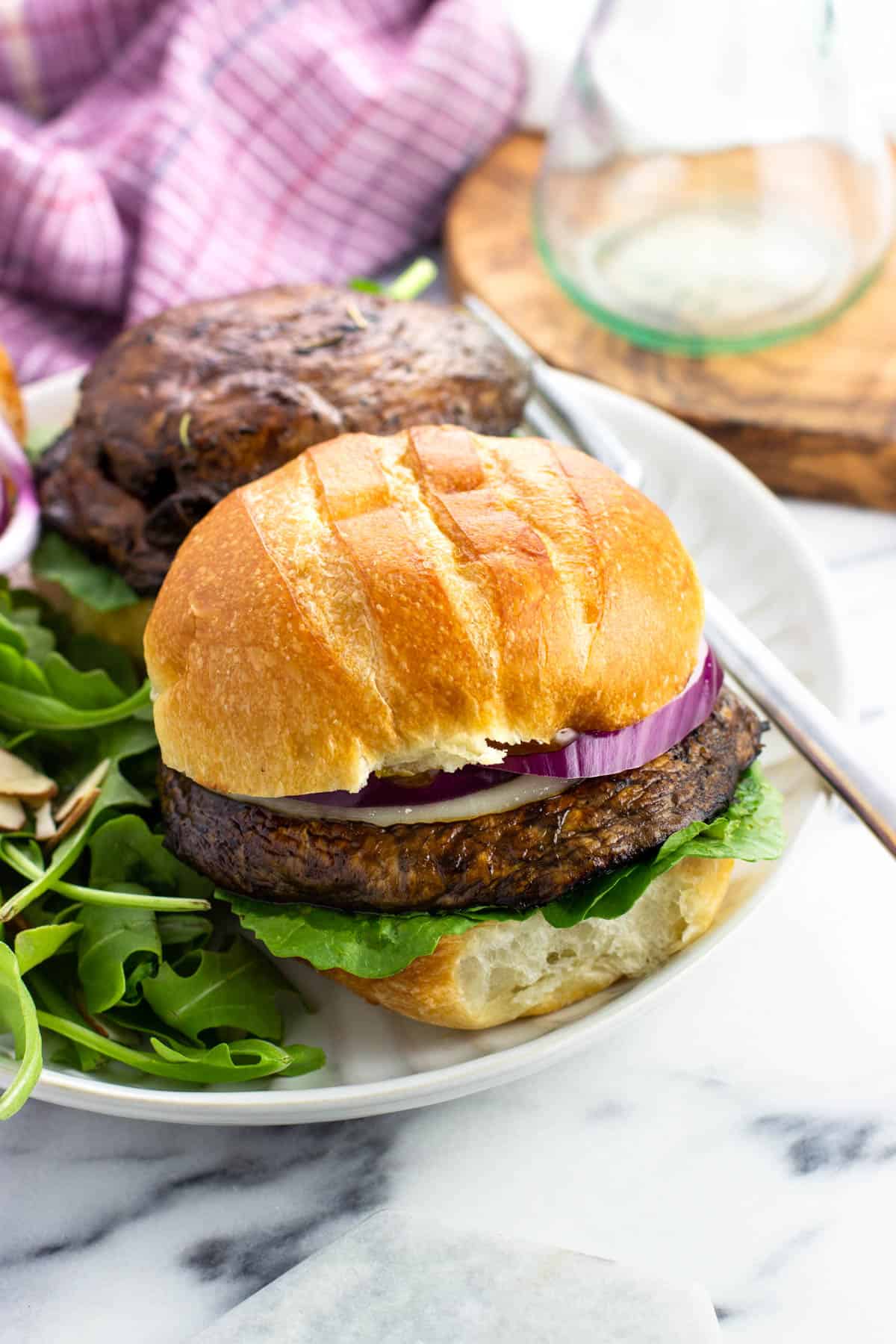 A portobello mushroom burger topped with cheese and red onion on a plate with a salad.