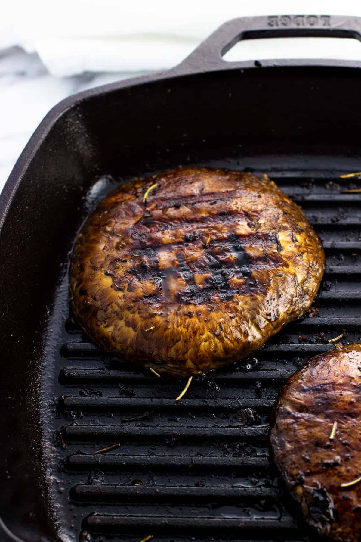 A marinated portobello mushroom cap on a cast iron grill pan with grill marks on the top.