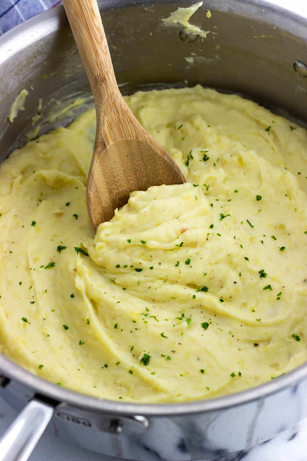 Mashed potatoes in a large metal pan with a wooden spoon.