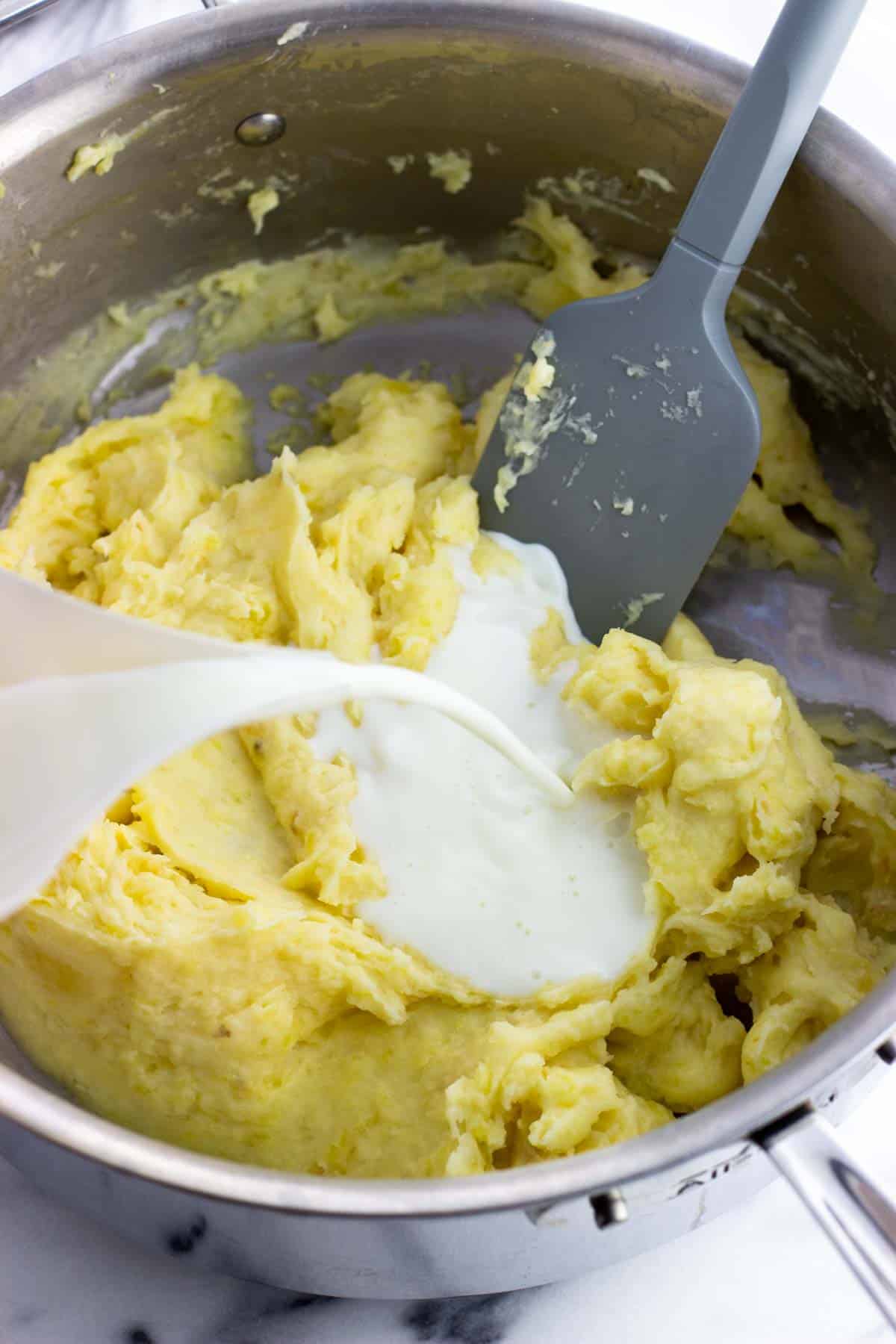 Milk being poured into the pan of roasted garlic mashed potatoes.