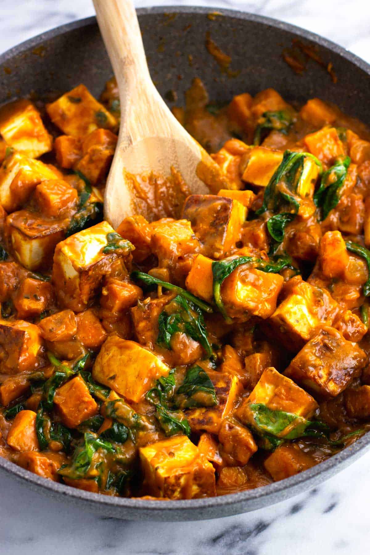 A skillet of paneer cubes, spinach, and sweet potatoes in simmer sauce.