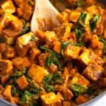 A skillet of paneer cubes, spinach, and sweet potatoes in simmer sauce.