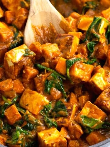 A skillet of paneer cubes, spinach, and sweet potatoes in simmer sauce.