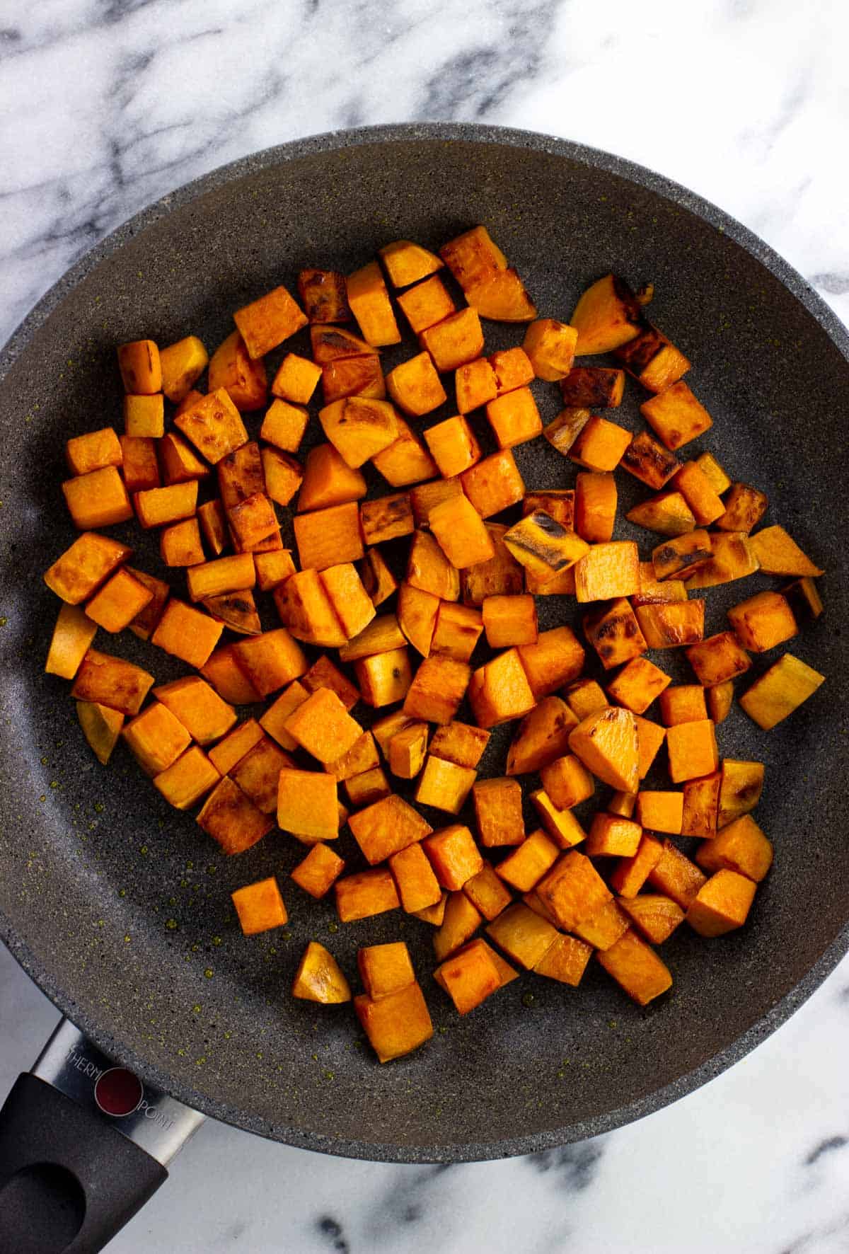 Sautéed sweet potato cubes in a skillet.