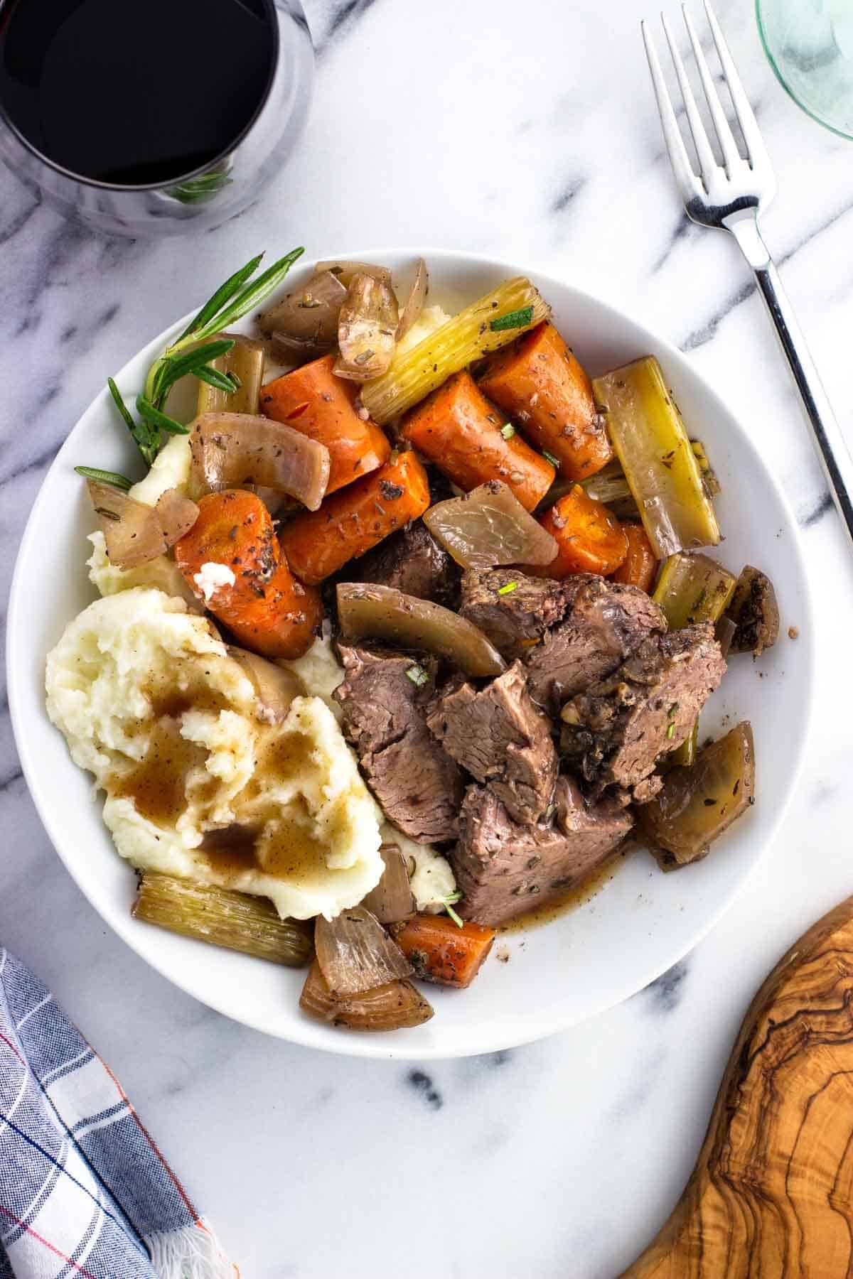 A shallow dish of sliced beef shoulder roast, vegetables, and mashed potatoes.
