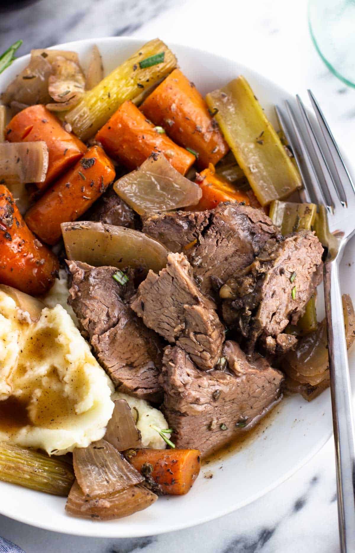 Chunks of beef on a plate with vegetables and mashed potatoes in gravy.