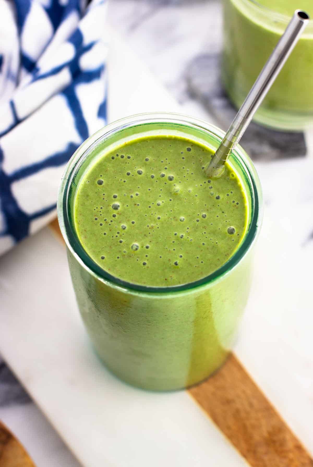 A green smoothie in a tall glass with a metal straw.