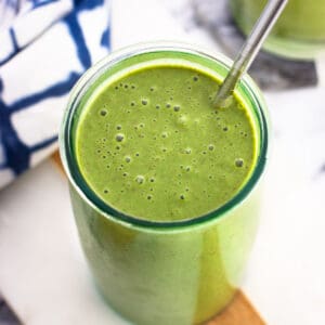 A green smoothie in a tall glass with a metal straw.