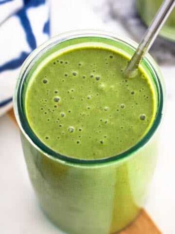 A green smoothie in a tall glass with a metal straw.