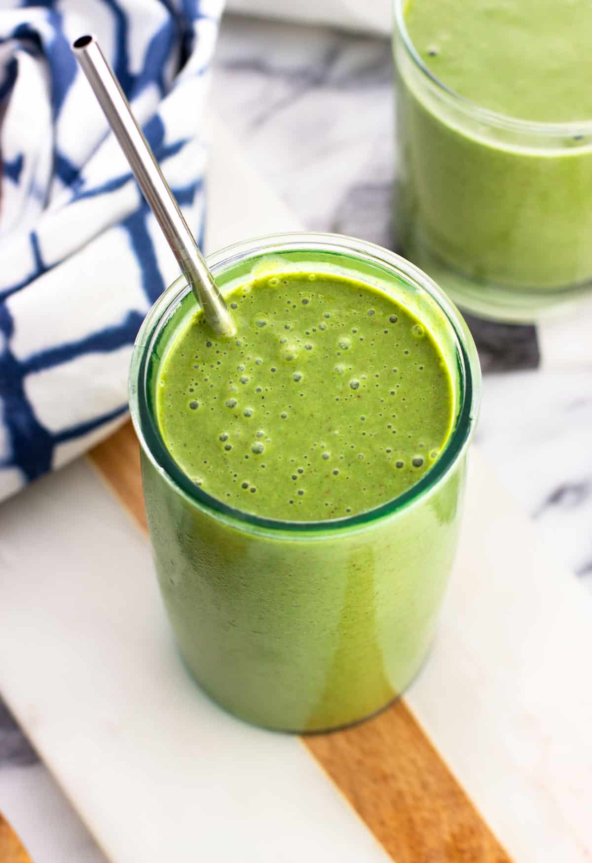 A green smoothie in a tall glass with a metal straw.