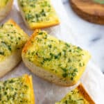 Pieces of roasted garlic bread on a piece of parchment paper.