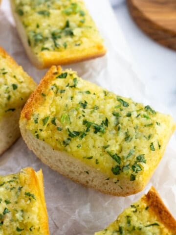 Pieces of roasted garlic bread on a piece of parchment paper.