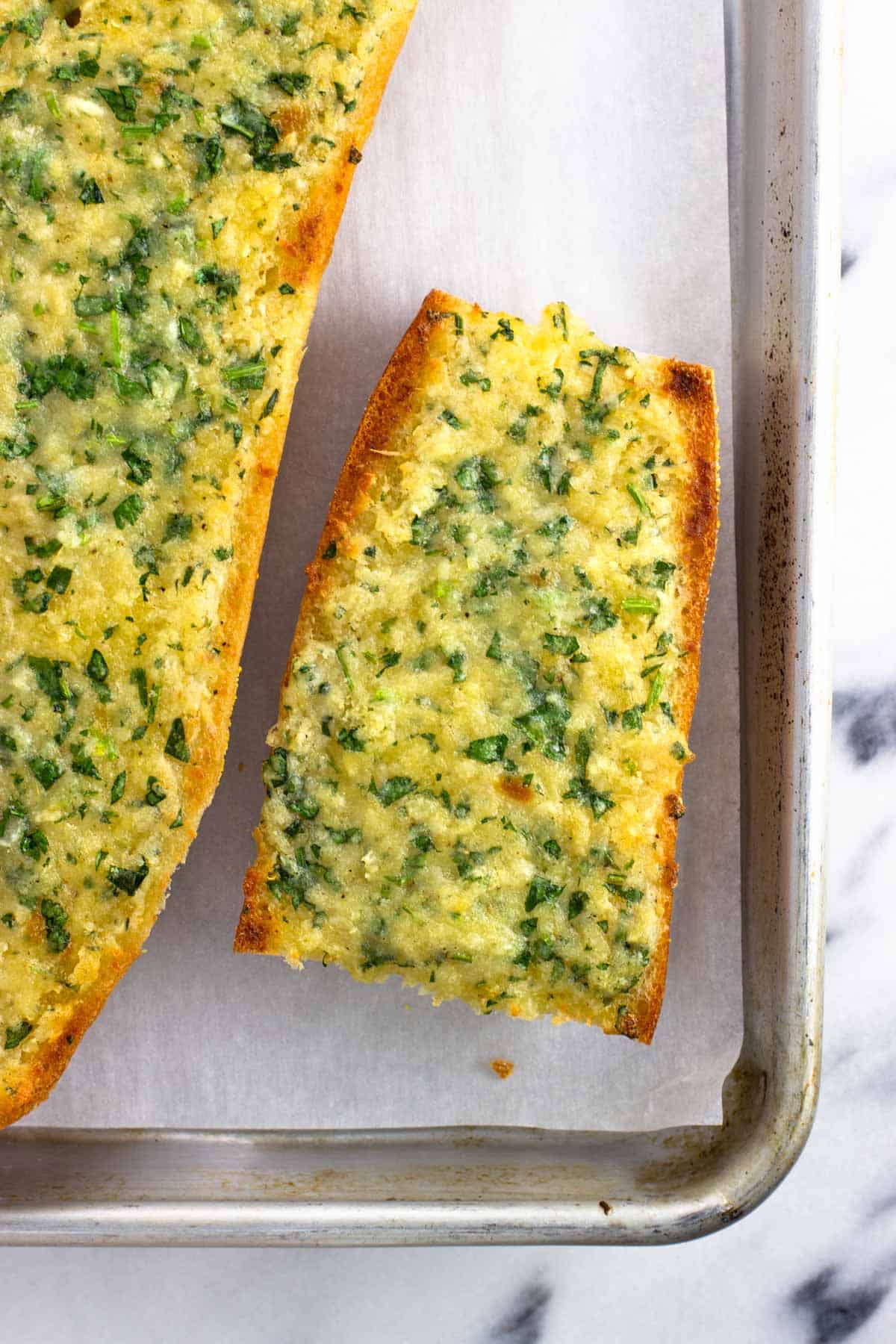 Slabs of whole roasted garlic bread on a baking sheet.