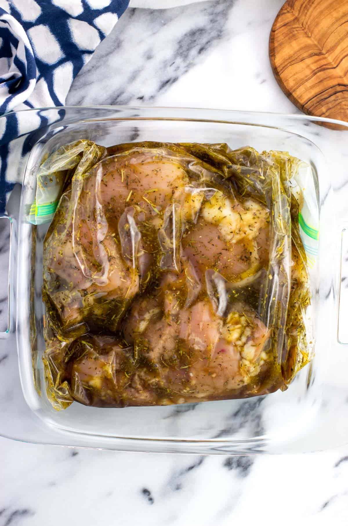 Chicken thighs marinating in a gallon-size bag contained in a glass dish.