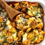 A wooden spoon scooping out a serving of baked tortellini from the dish.