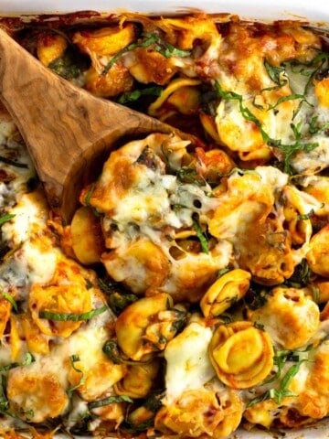 A wooden spoon scooping out a serving of baked tortellini from the dish.