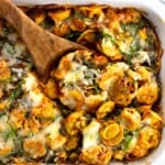 A wooden spoon scooping out a serving of baked tortellini from the dish.