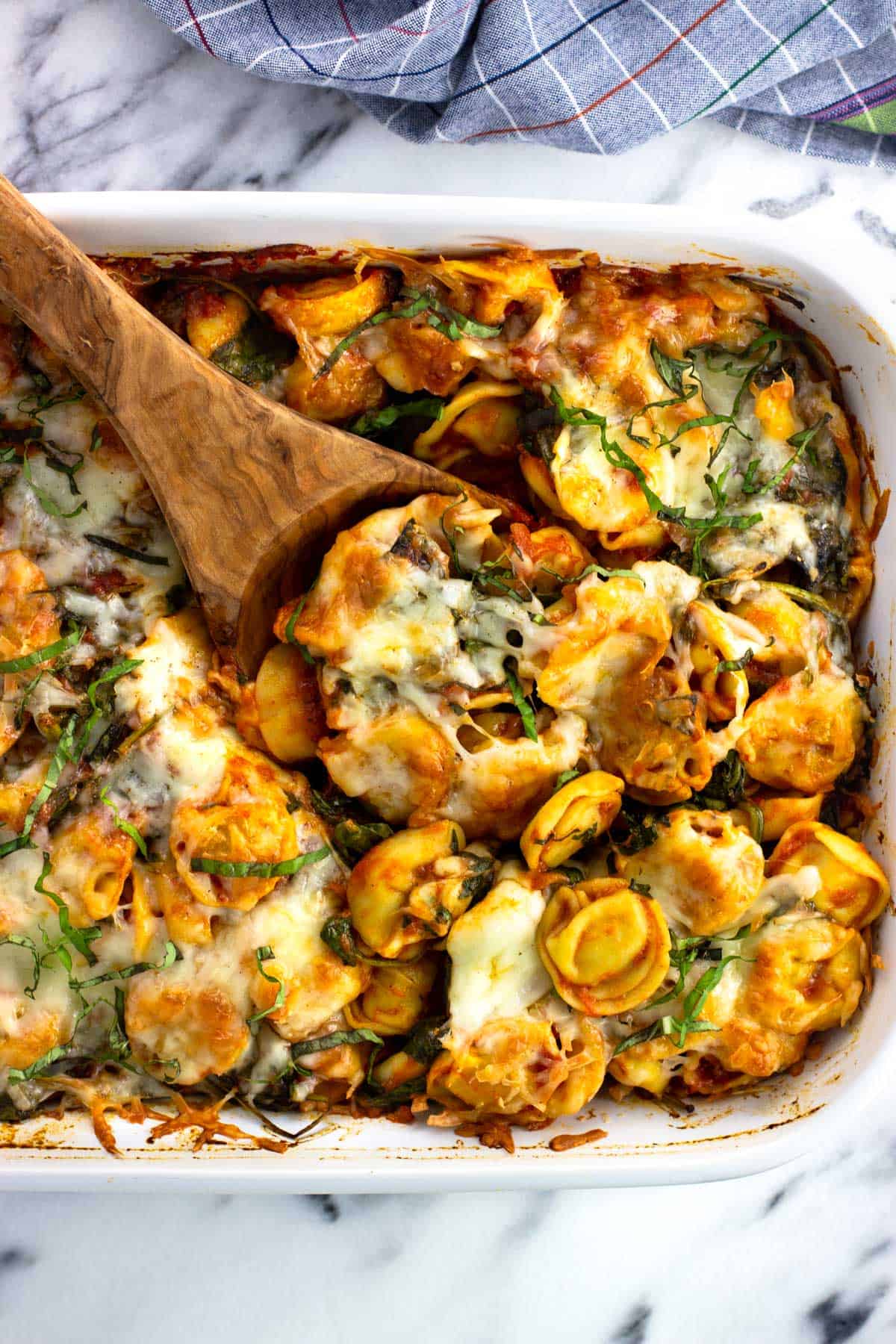 A wooden spoon scooping out a serving of baked tortellini from the dish.