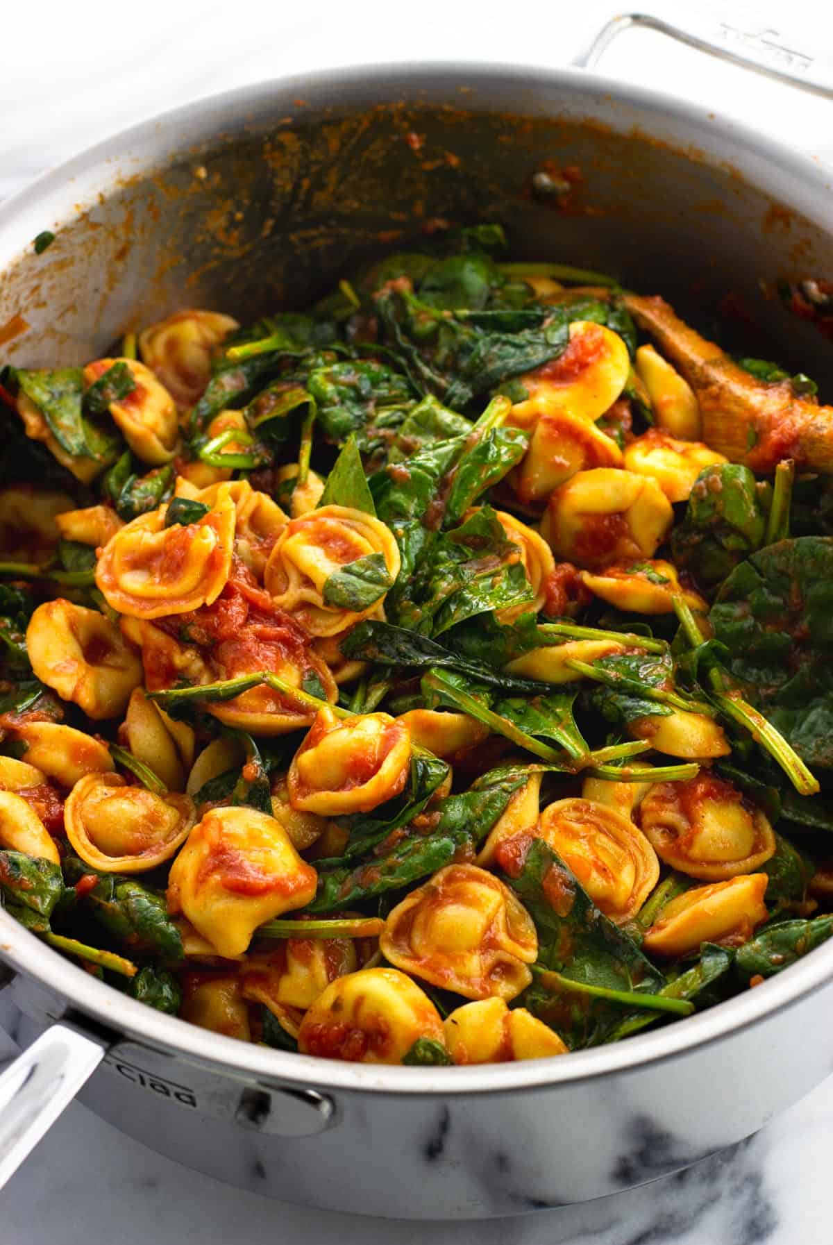 Cooked tortellini, marinara, and spinach in a large pan.