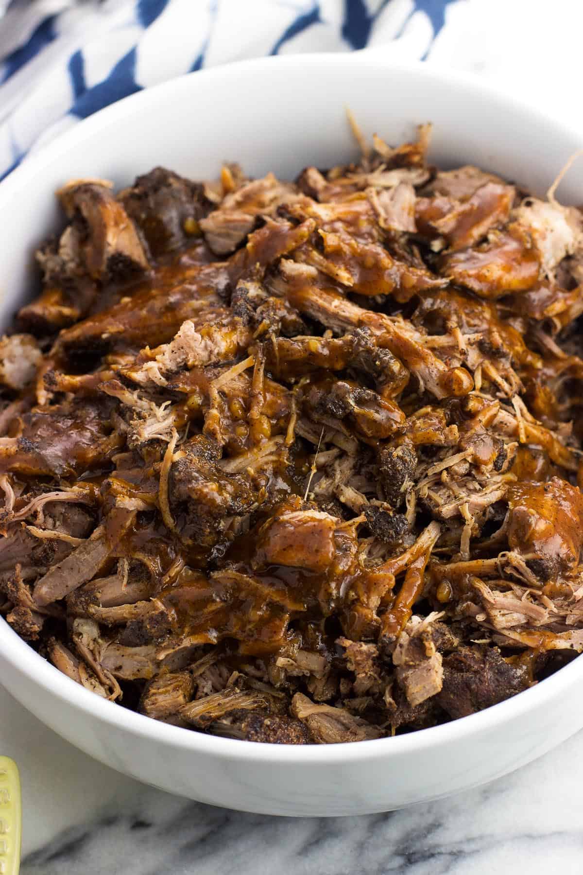 A serving bowl of coffee-rubbed pulled pork drizzled with BBQ sauce.